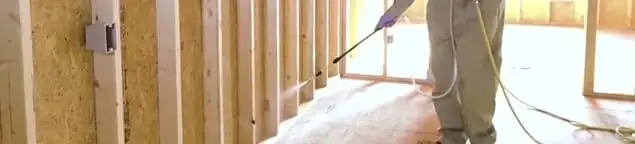 Termite treatment technician applying spray along framing and unfinished walls in El Paso, TX